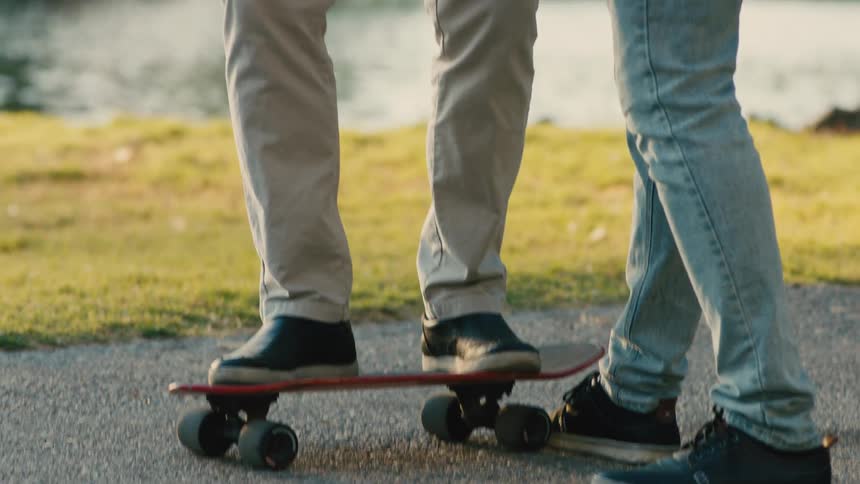 A young man helping an older man onto a small skateboard and they are both happy