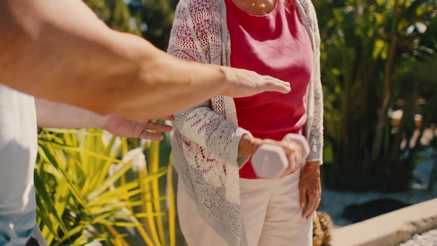 Man helping an elderly lady do dumbbell lifting