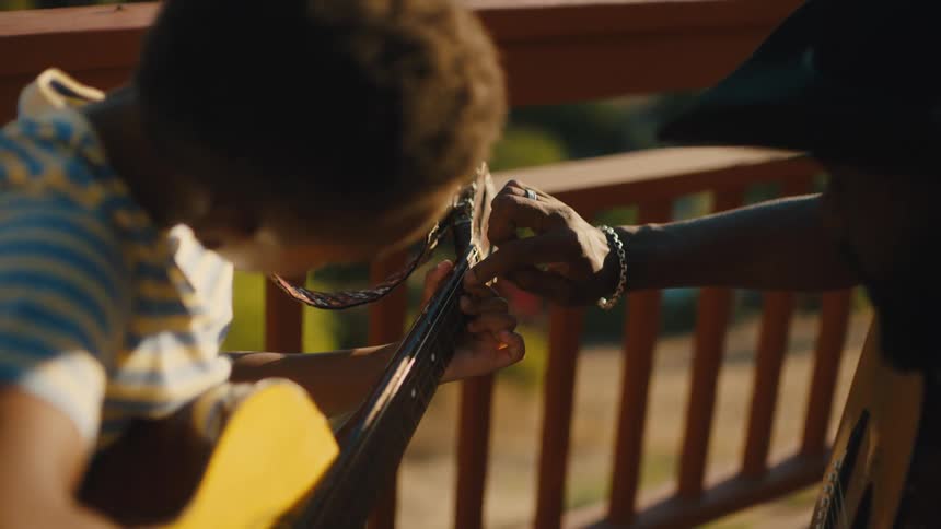 Man helping a boy tune the strings of a guitar