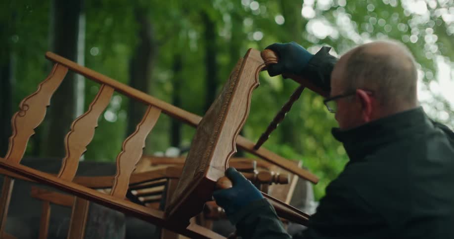 Man placing a wooden chair on top of others in an outdoor location