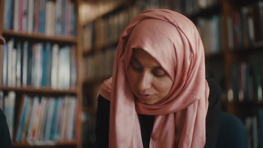 Woman with pink headscarf holding pen on paper while standing in library