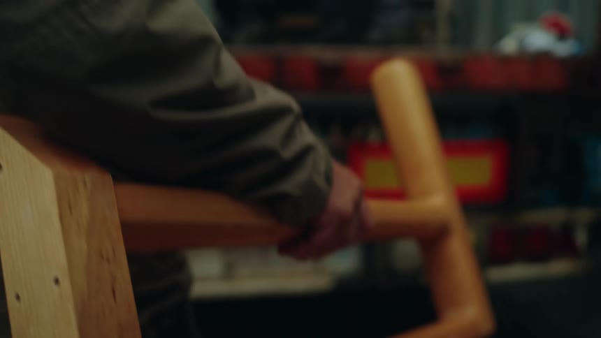 Close up of a man carrying a wooden piece of furniture and handing it to another man who is moving the furniture with other men