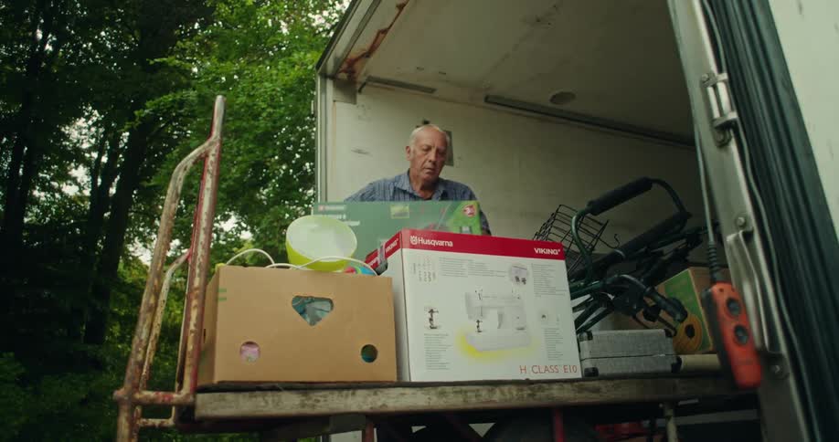 An elderly man unloads items from a removal truck and stacks them onto a cart