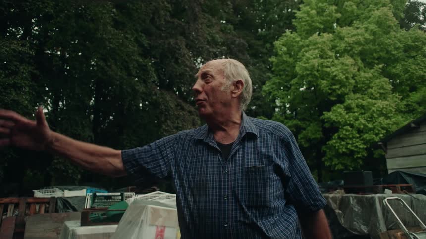 An elderly man is talking while gesturing with his arm