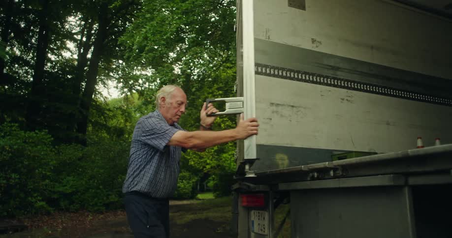 An old man closes the back door of a cargo truck