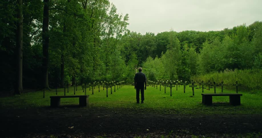 A man stands still in a cemetery on a cloudy summer day