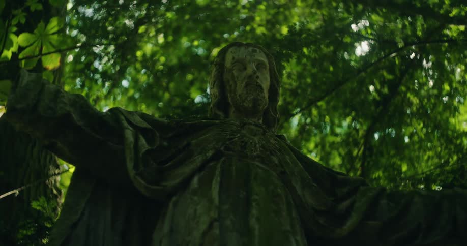 Statue of jesus christ with open arms beneath a tree