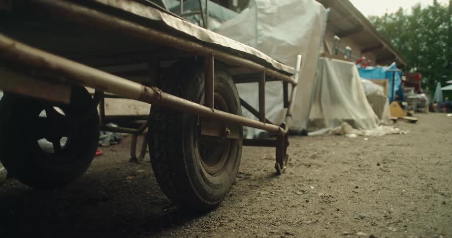 Wheel of a cart parked in a yard with a shed and items under tarp in the background