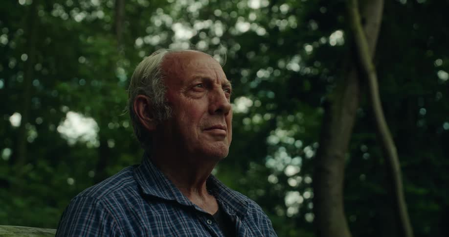 Close up of the face of an elderly man sitting on a bench looking sad
