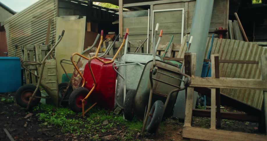 Collection of wheelbarrows stacked against a shed