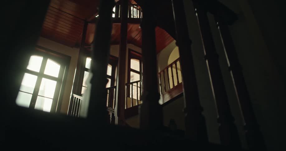 Indoor staircase with wooden banisters leading up to a landing with doors and windows