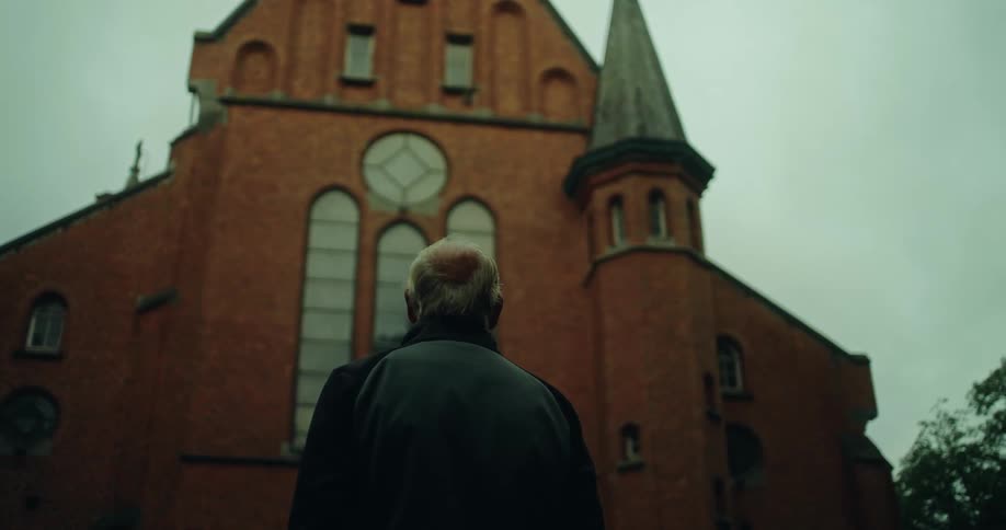 The back of an elderly man standing looking up at a church