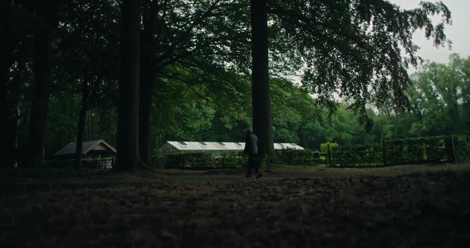 Silhouette of an Elderly man walking in a forest towards a greenhouse