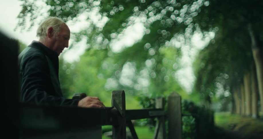 Elderly man opening a wooden gate and entering