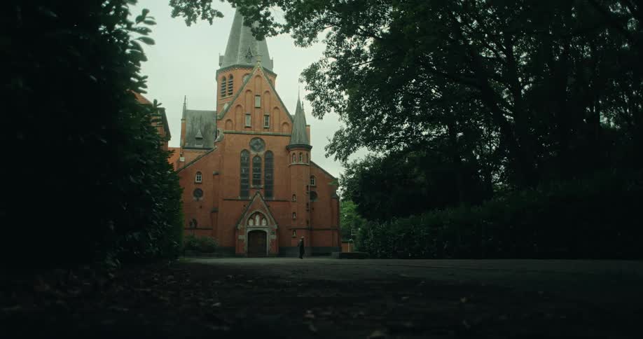 A man walks past a large brick church with a pointed steeple under an overcast sky