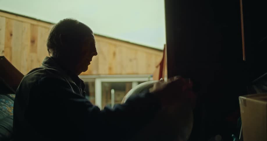 A silhouette of an older man grabbing a globe off a shelf in an open barn