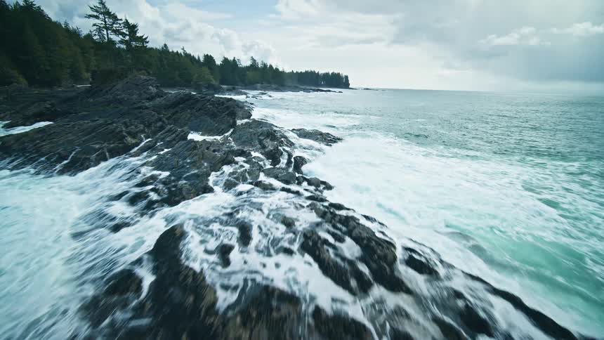 Aerial of coastal waters crashing against rocks on the coast in the middle of the day