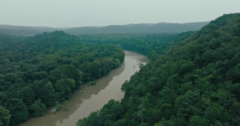 A dark brown river runs between heavily forested hills
