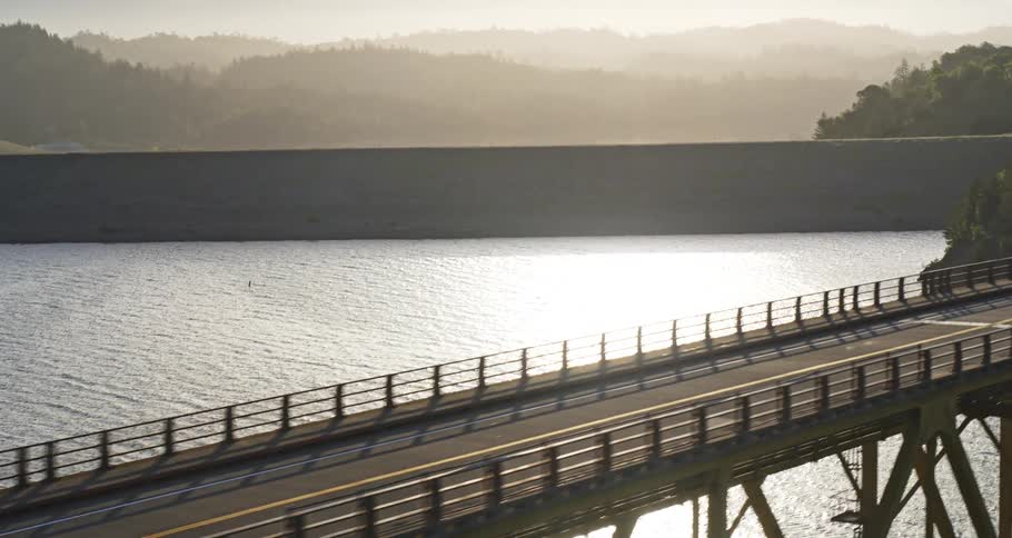 A suspension bridge over an artificial lake caused by a dam and there is an asphalt road on top of the tip