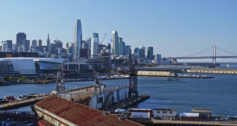 A cityscape with a modern stadium cranes and a bridge overlooking a body of water with a clear blue sky