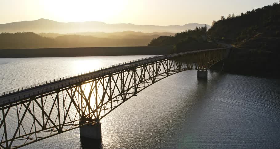 An aerial view of a huge suspension bridge over a large lake with cars passing over it