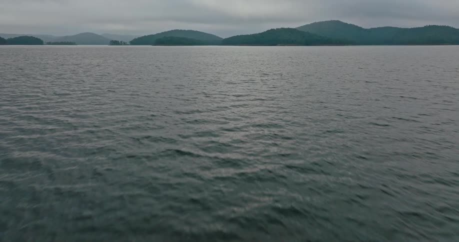 A calm dark colored lake or reservoir with a hazy mountain range in the background