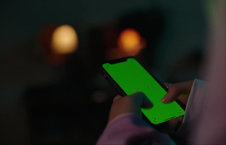 A woman taps away on a smartphone with a green screen