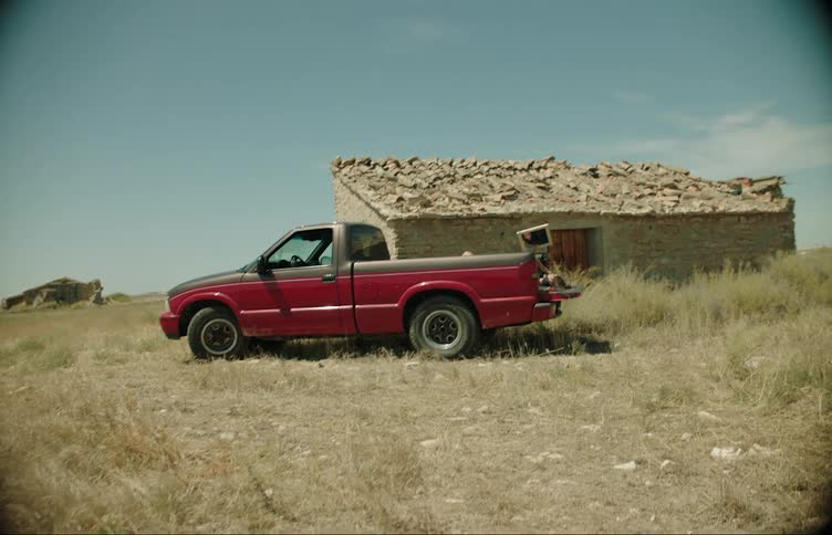Red and black car with a dump truck on the back parked next to a house in pedras