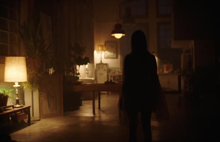 Woman silhouetted against the light in a dimly lit room stops walking and stands