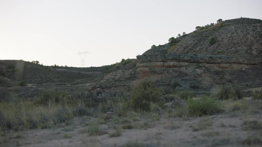 Scrub dotted hills border arid plains under a cloudy sky