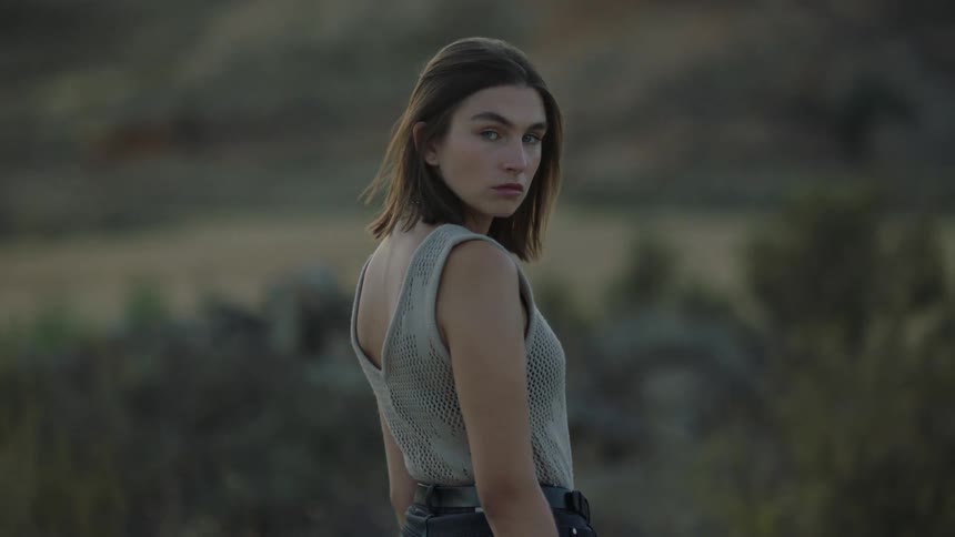 A young woman stands with her back turned and then she turns her face and stares straight ahead and turns back again