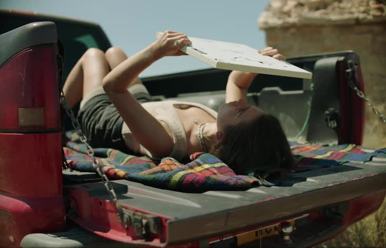 Woman lying in the back of a red pickup truck looking at herself in a mirror