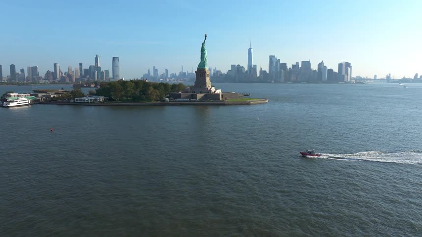 A boat sailing on the water near the statue of liberty and behind it there is a big city with tall buildings