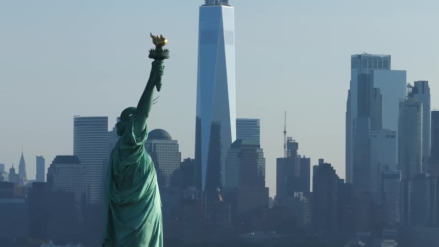 The statue of liberty is behind there are several skyscraper buildings of a metropolitan city