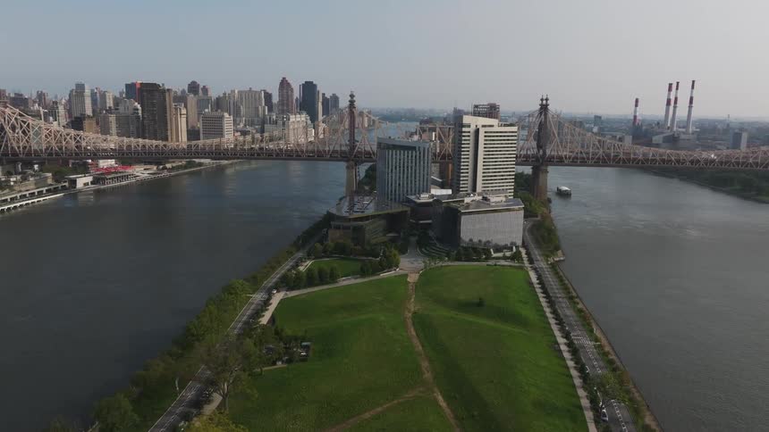 A large green park with two roads on the sides and it is in the middle of the water with a bridge that connects two points of a metropolitan city