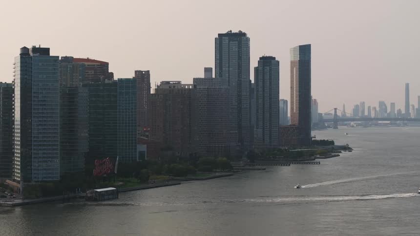 A metropolitan city with huge buildings facing the water with a few boats passing by