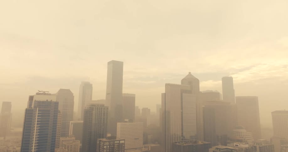 Tilt down reveal of a city skyline enveloped in brown wildfire smoke