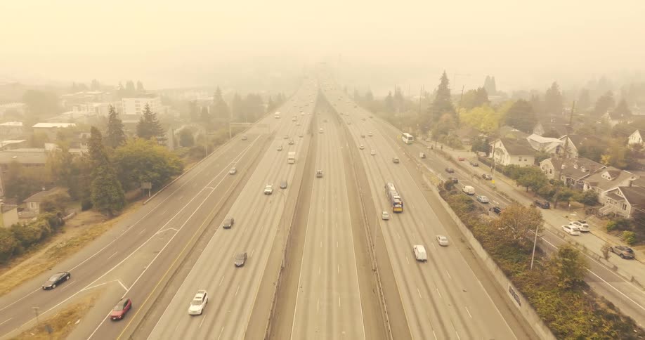 Traffic moves along a freeway passing through a residential area under extremely dense wildfire smoke