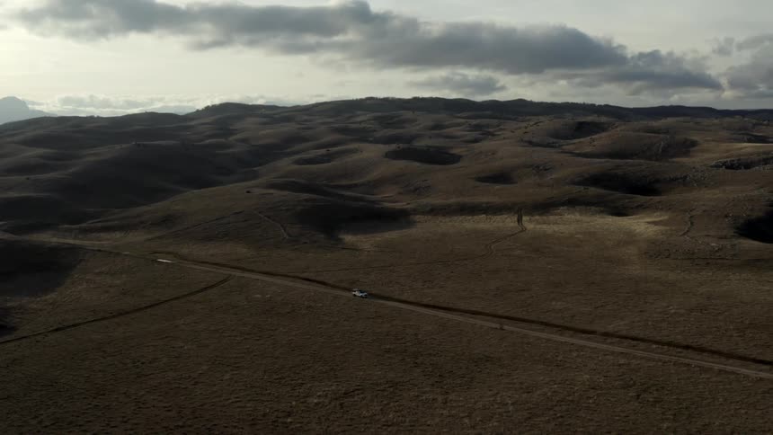Vehicle drives along highway passing through hills and a grassland