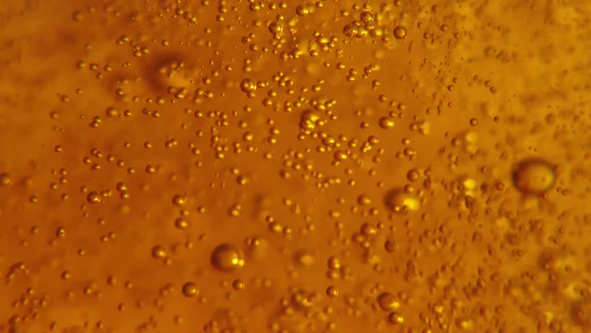 Closeup view of bubbles and foam in a goldenbrown liquid with light reflecting through it creating an amber glow