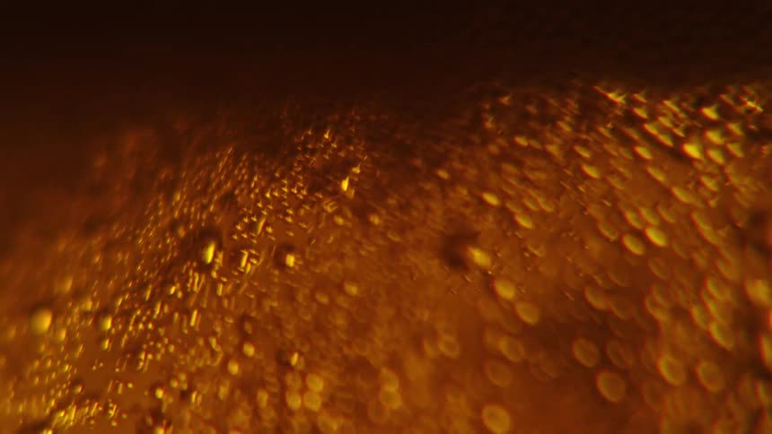 Closeup view of bubbles and foam in a goldenbrown liquid with light reflecting through it creating an amber glow