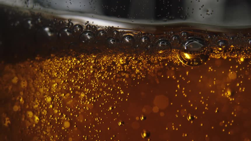 Gas bubbles inside beer rising up to the foam as more beer is poured into the container