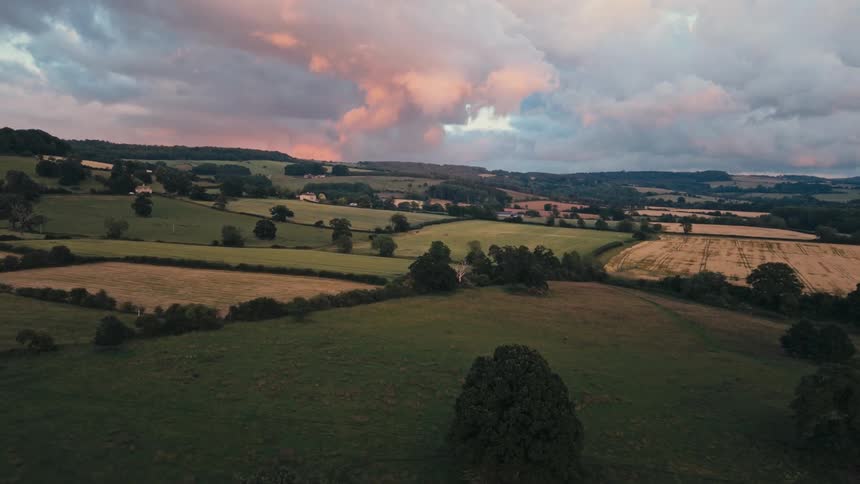 A sky with pink and orange hues over a landscape of green and plowed fields