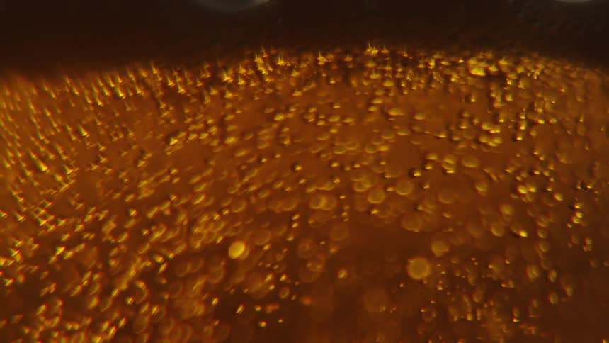 Closeup view of bubbles and foam in a goldenbrown liquid with light reflecting through it creating an amber glow