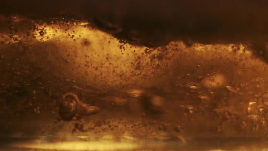 Closeup view of bubbles and foam in a goldenbrown liquid with light reflecting through it creating an amber glow