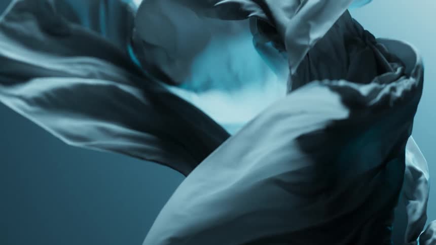A close up shows flowing textured fabric in a blue toned color moving in slow motion
