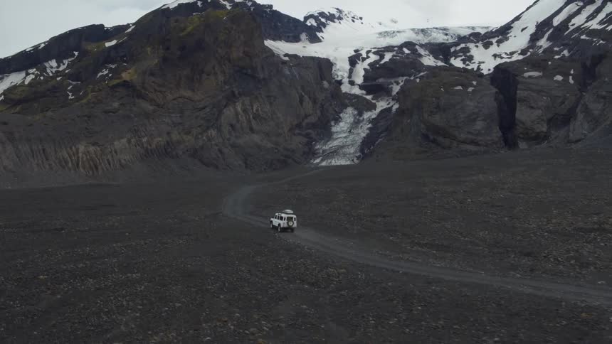 Suv rolling down a dirt road towards snow-covered mountains