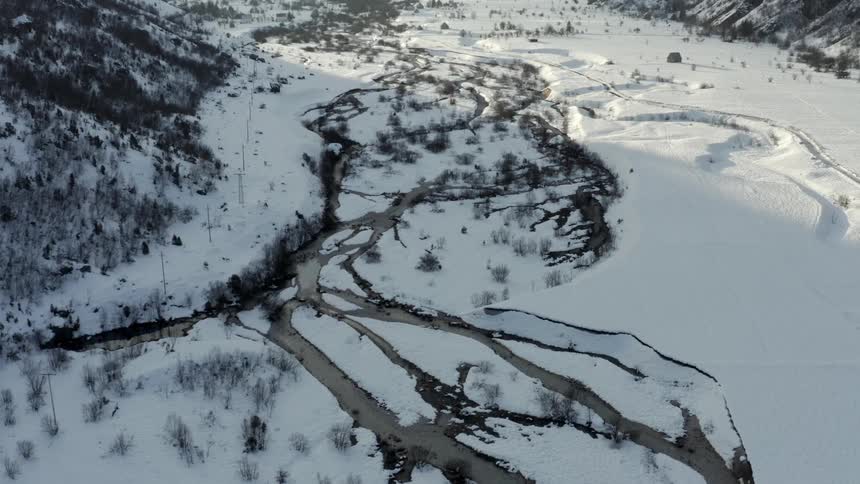 Branching streams flow across the snowy valley between forest covered slopes during winter