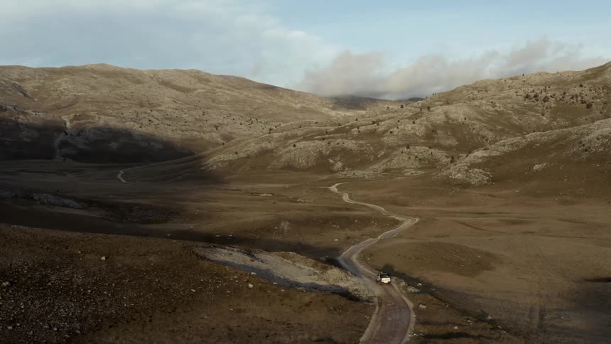 A truck drives on the dirt road toward the mountains