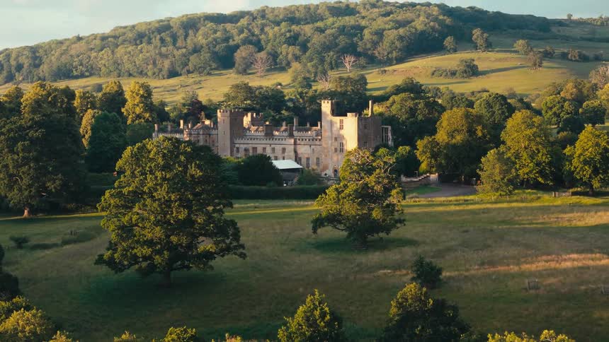 Manor house stands nestled among trees at the base of a hill in the rural countryside